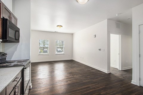A kitchen with a microwave on the wall and a wooden floor.