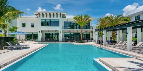 a large swimming pool with chaise lounge chairs and palm trees in front of a white building