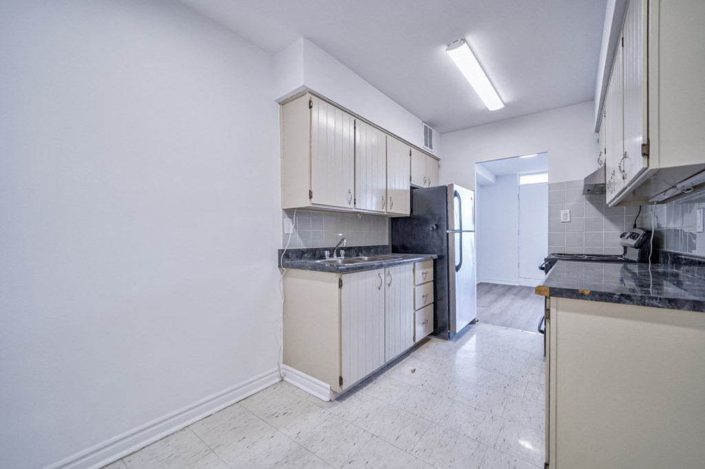 a kitchen with white cabinets and black counter tops and a refrigerator