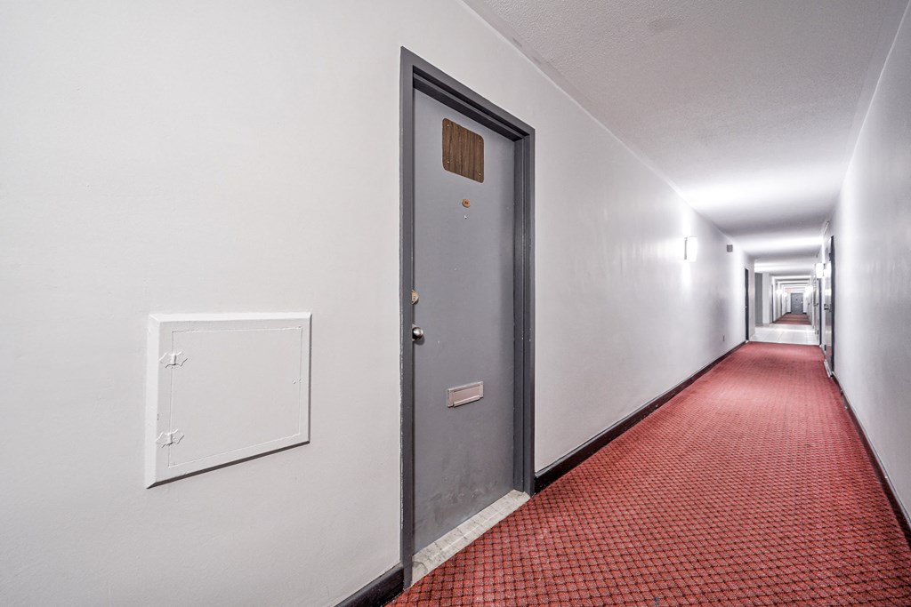 a corridor with a door and a red carpet and white walls