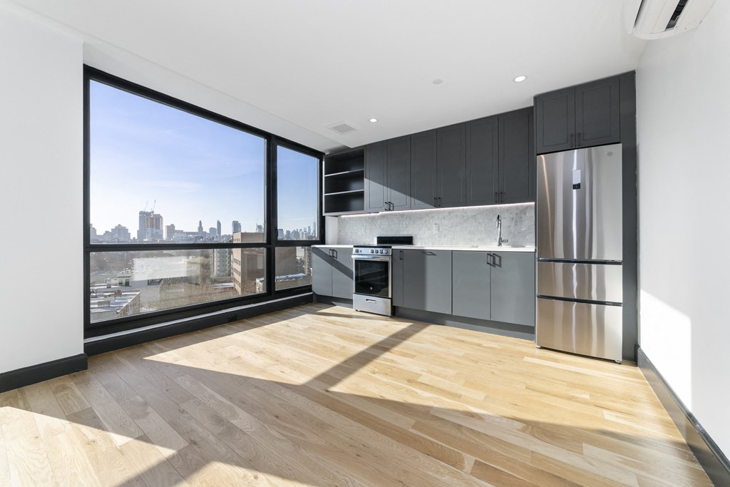 A modern kitchen with wooden floors and a city view through the windows.