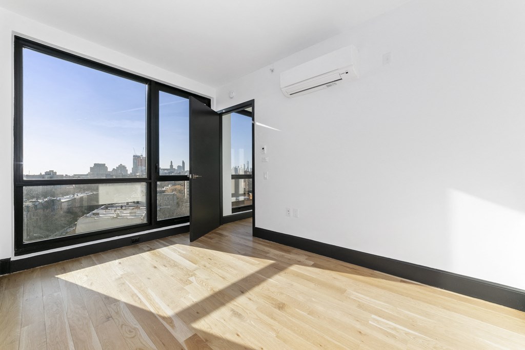 A room with a wooden floor and a large window overlooking a cityscape.