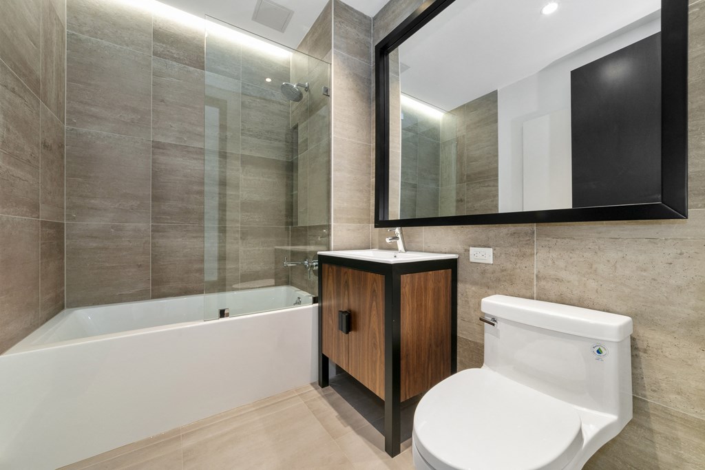 A modern bathroom with a white bathtub, wooden cabinet, and a white toilet.