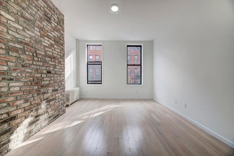 an empty living room with a brick wall and wood floors