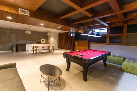 A pool table is in the middle of a room with a round table and a couch.