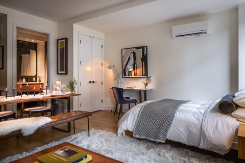 A bedroom with a bed, a chair, a table, and a mirror.