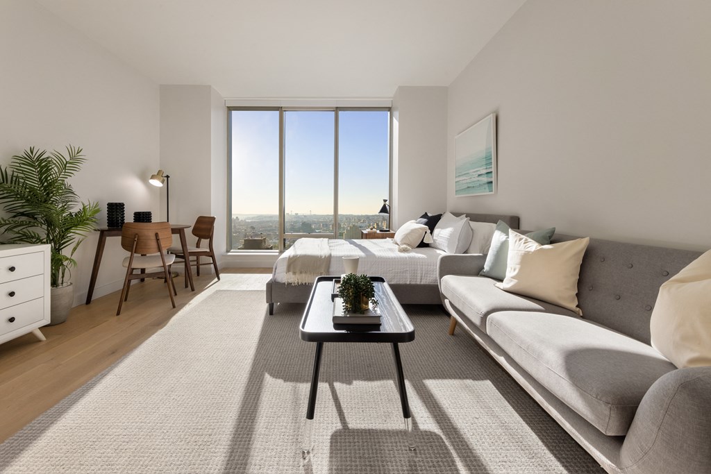 a living room with a couch and a table and a large window at The Paxton, Brooklyn, 11201