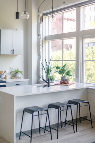 a kitchen with a white counter top and three black stools in front of a window at The 22 Apartments, St. Louis, MO 63103