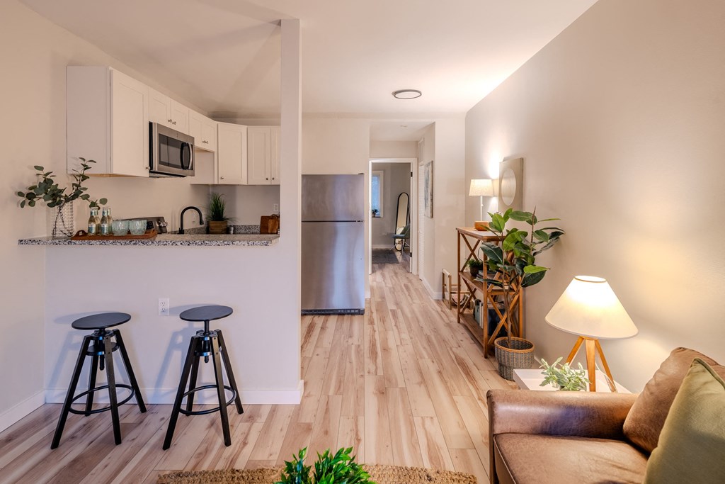 a living room with stools and a kitchen with a refrigerator