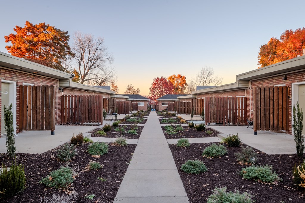 a pathway between two rows of brick buildings with plants and trees