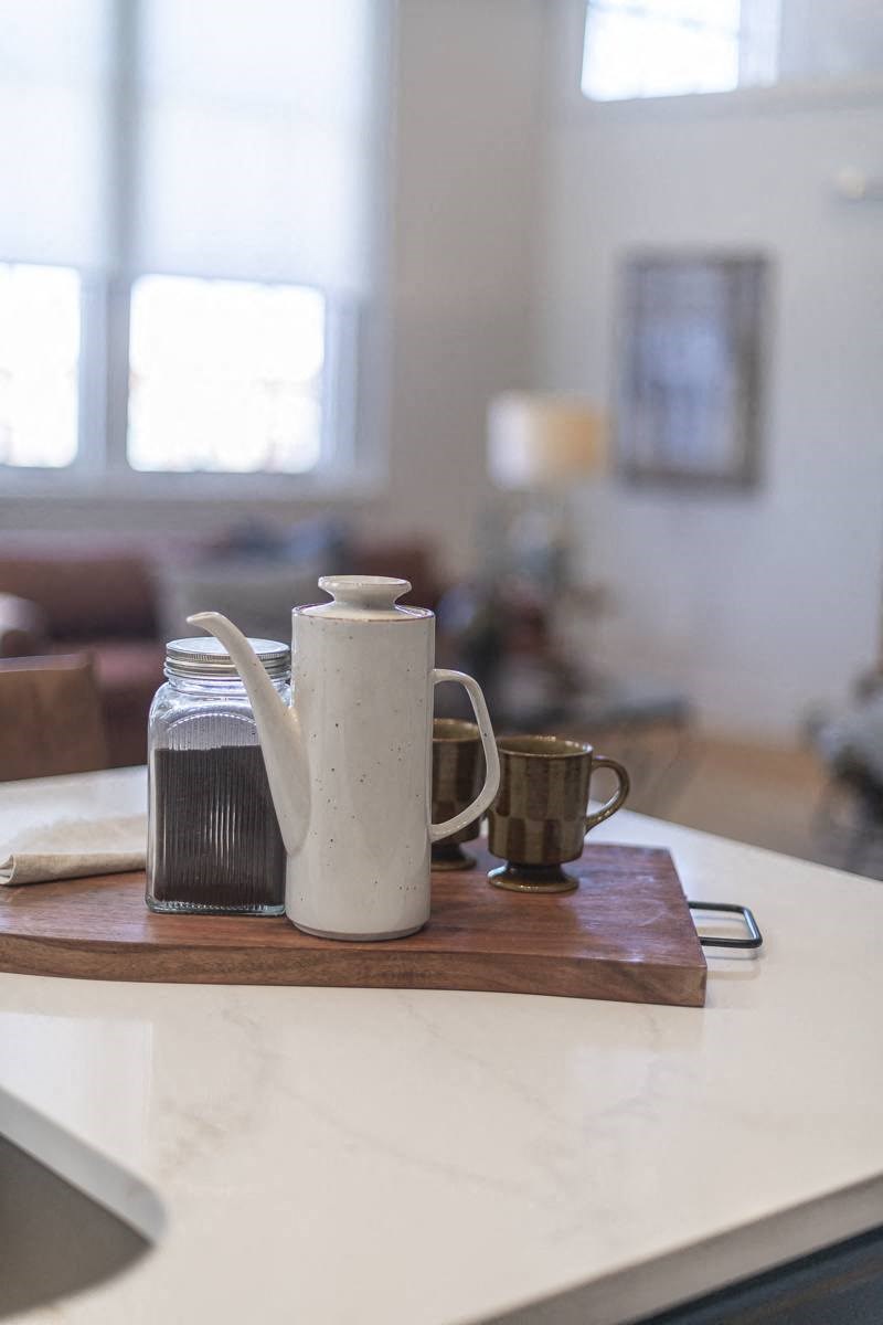 a coffee pot and cup on a cutting board on a kitchen counter