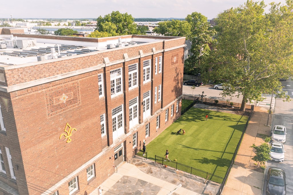 an aerial view of a brick building with a lawn and trees