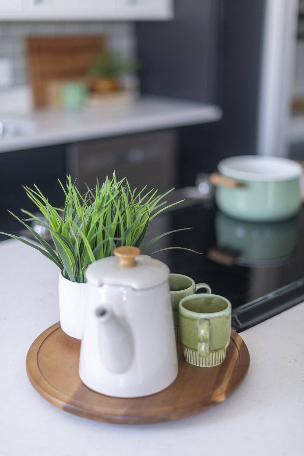 a white teapot with a plant and three cups on a wooden tray