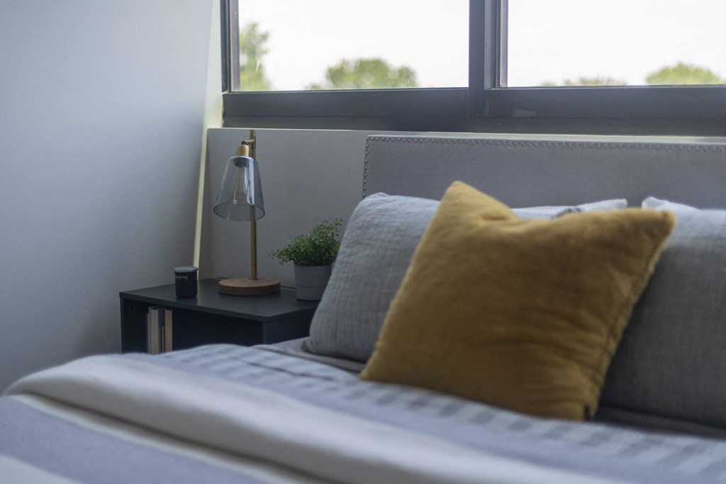 a bed with a yellow pillow in a room with a window