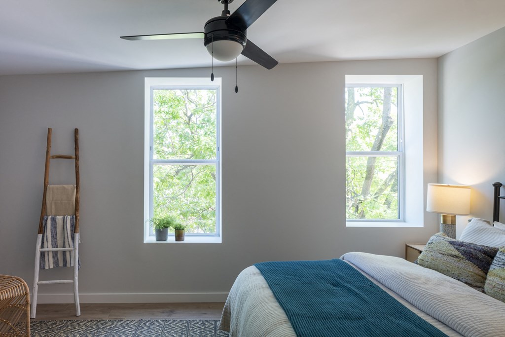 a bedroom with a bed and a ceiling fan and two windows