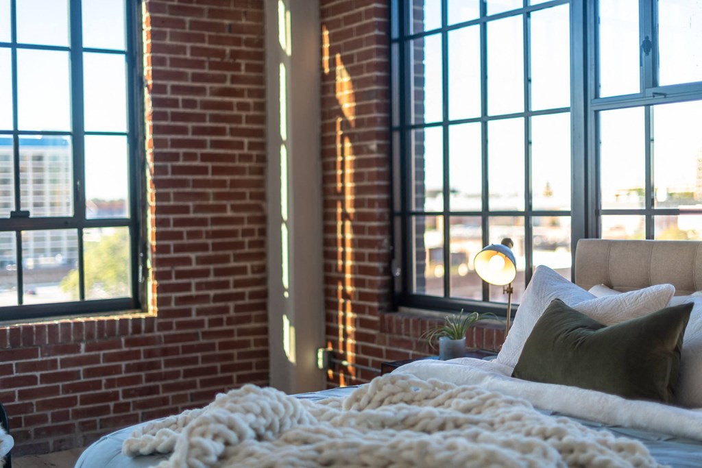 a bedroom with large windows and a bed in front of a brick wall at The 22 Apartments, Missouri
