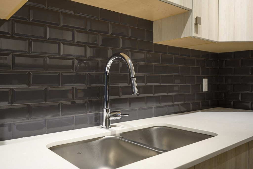 a stainless steel sink in a kitchen with black tiles
