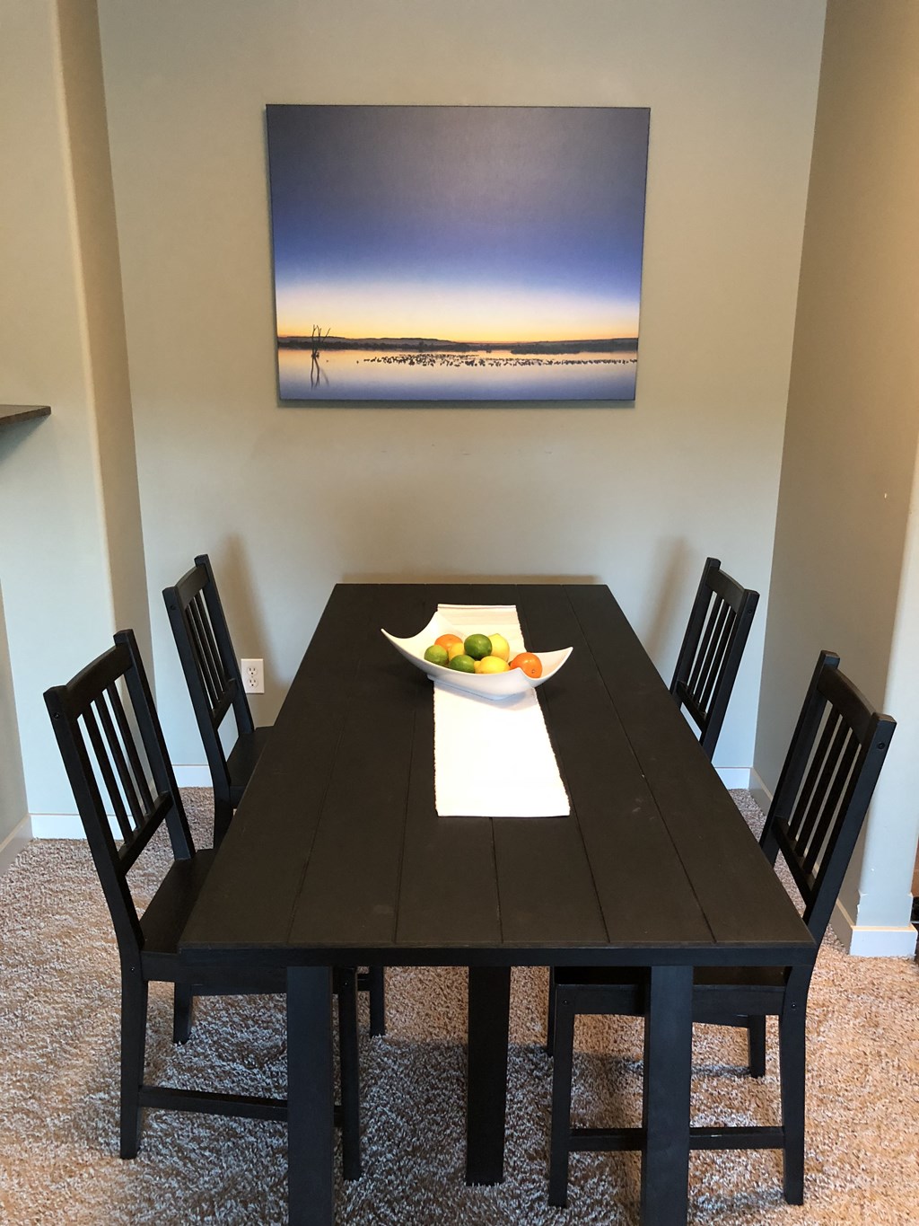 A black dining table with a bowl of fruit on it and four chairs.