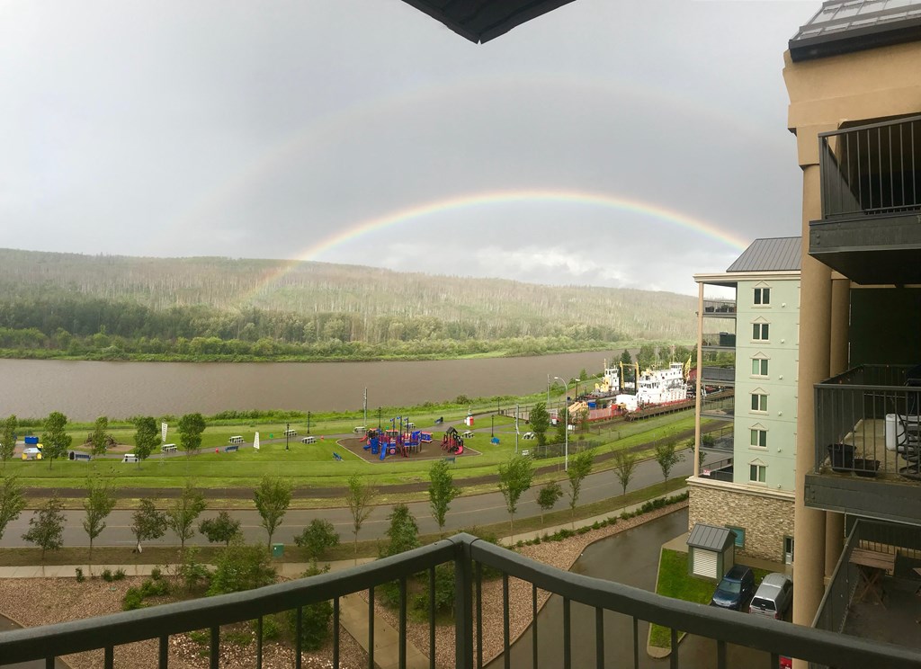A rainbow appears over a lake with a building and playground in the foreground.