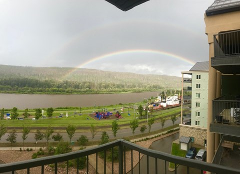 A rainbow appears over a lake with a building and playground in the foreground.