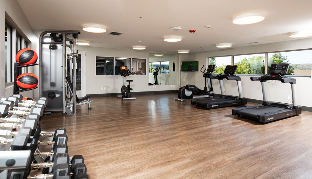 a gym with cardio machines and weights on a wooden floor