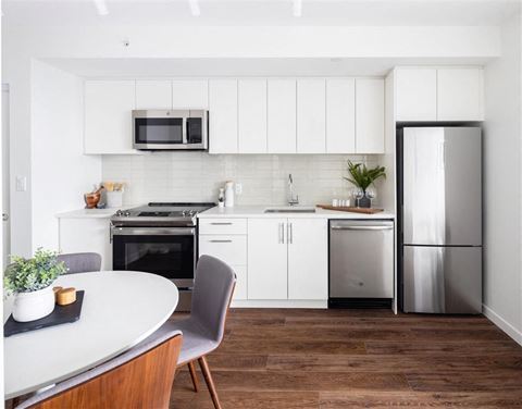 a white kitchen with stainless steel appliances and a table