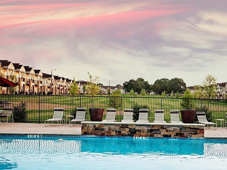 A swimming pool with sun loungers and a row of houses in the background.