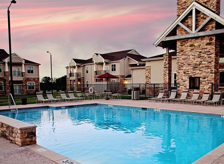 A swimming pool surrounded by a stone wall and lounge chairs.