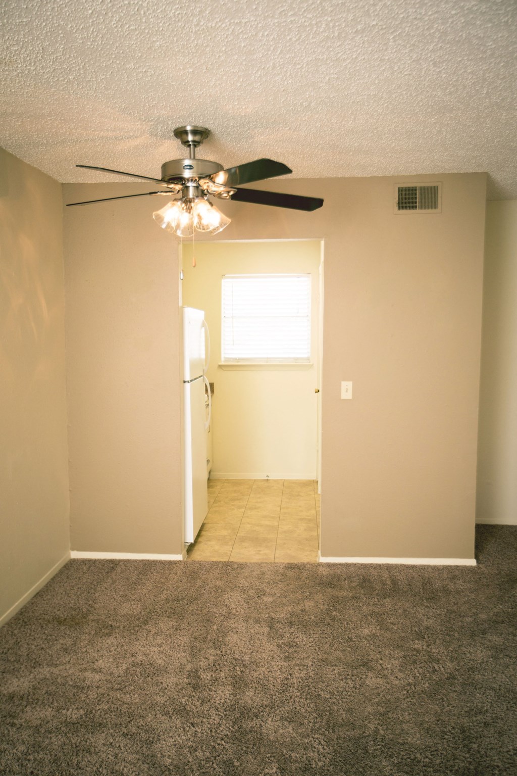 an empty living room with a ceiling fan and a door to a kitchen