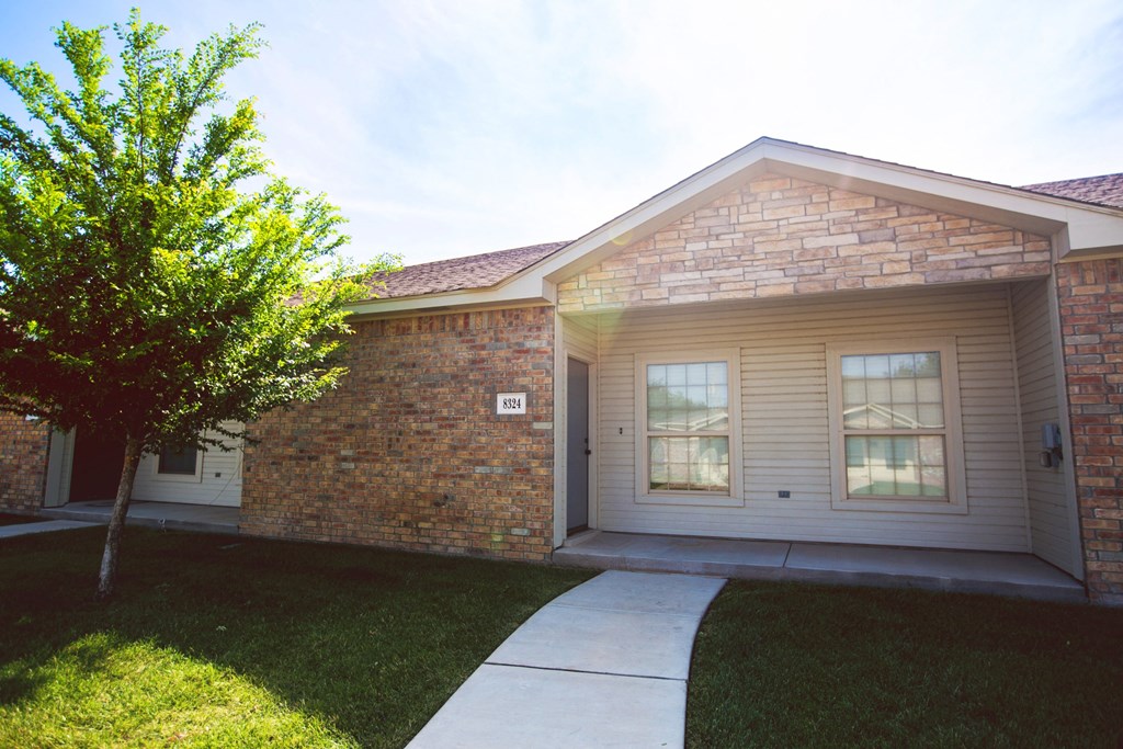 the front of a brick house with a sidewalk and grass
