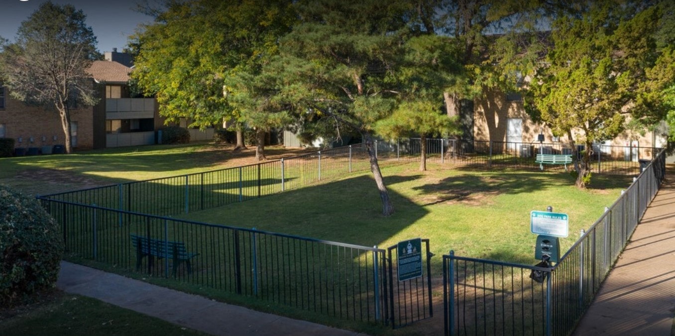 a park with benches and a fence in front of an apartment building