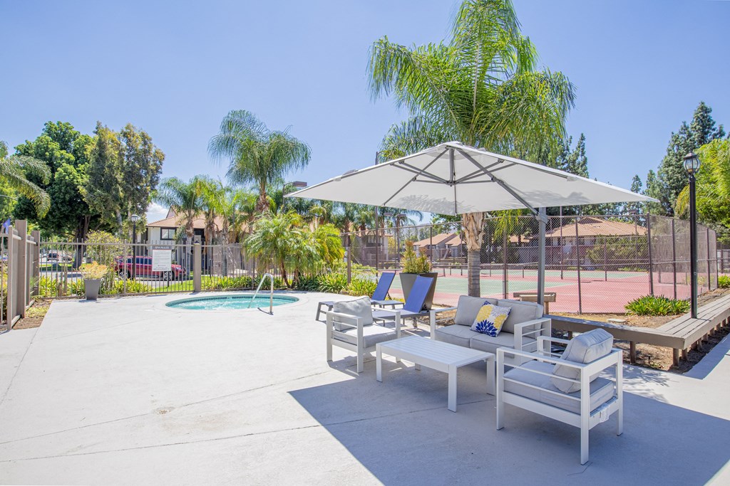 a patio with two lounge chairs and an umbrella with a pool in the background