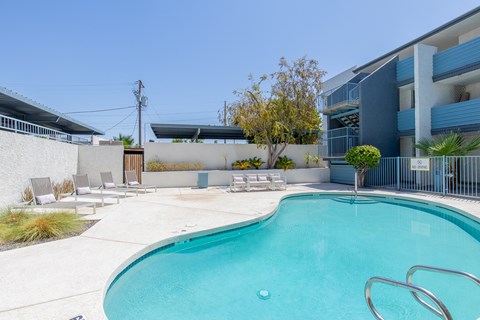 a swimming pool with chaise lounge chairs and a tree in front of a blue building