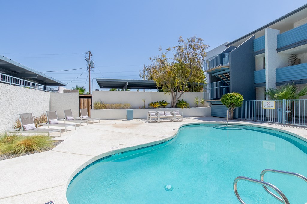 a swimming pool with chaise lounge chairs and a tree in front of a blue building