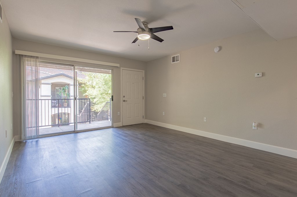 an empty living room with a sliding glass door and a ceiling fan