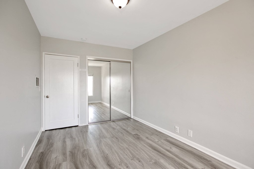 a bedroom with white walls and wood flooring and a door to a hallway