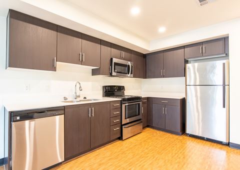 an empty kitchen with stainless steel appliances and wooden floors