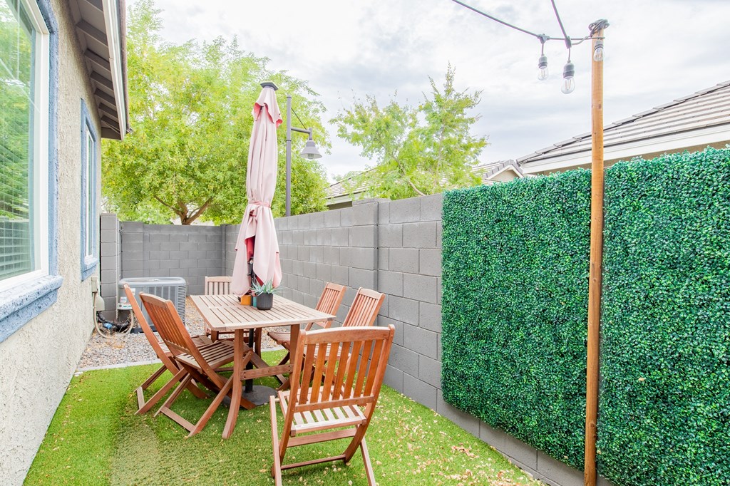 a backyard patio with a table and chairs and a privacy hedge