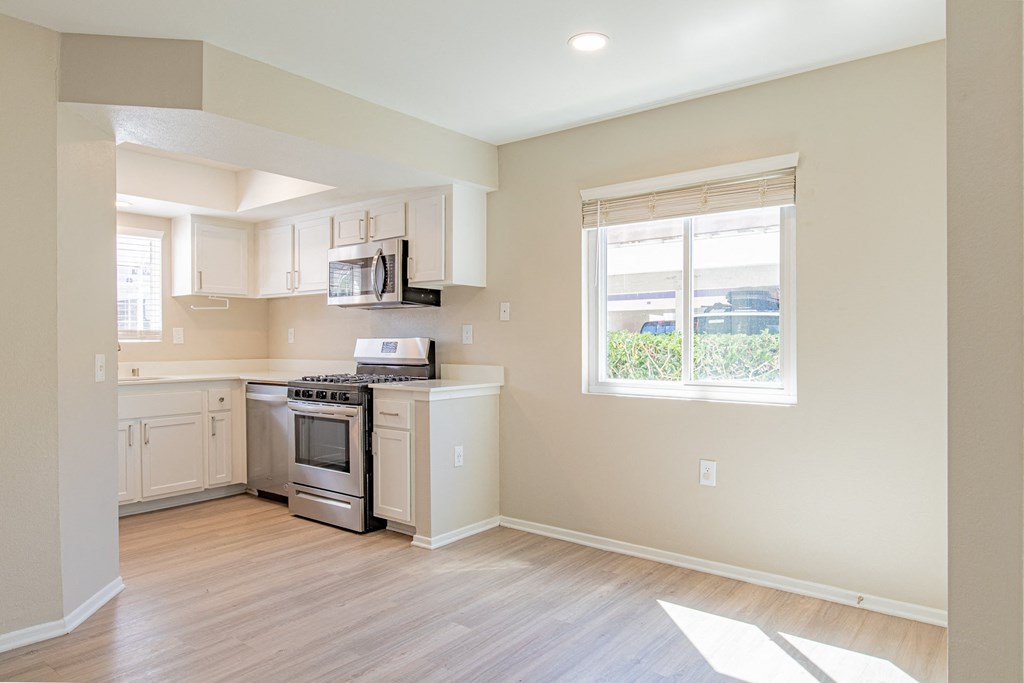 an empty kitchen with white cabinets and a window