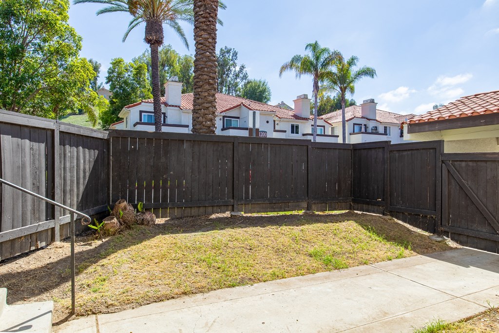 a fenced in yard with palm trees and a house in the background