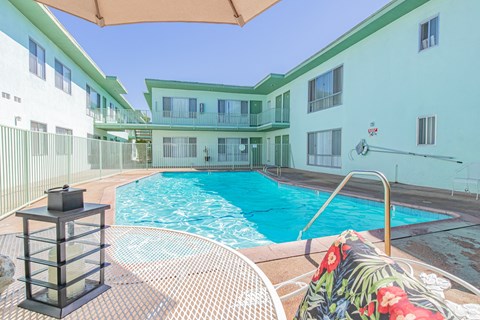 A pool surrounded by a white fence and a chair with a floral cushion.