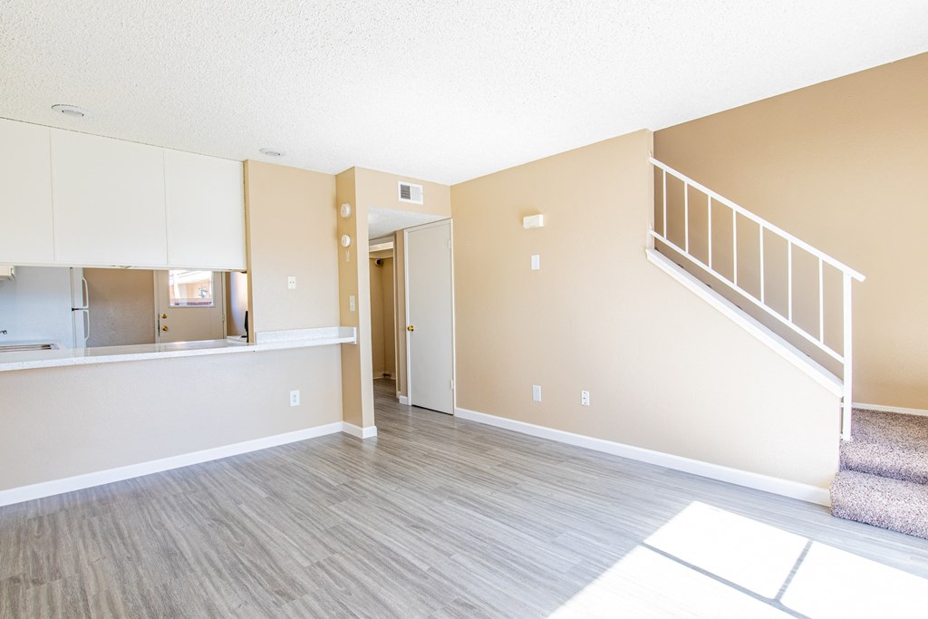 an empty living room with a staircase and a kitchen