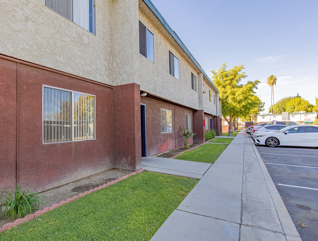 a side view of a building with a sidewalk and cars parked