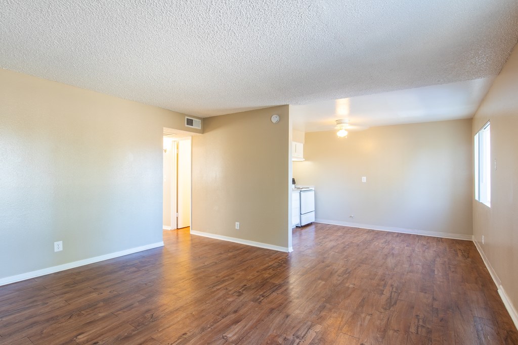 an empty living room with wood flooring and a kitchen