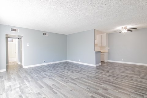 an empty living room with wood flooring and a kitchen