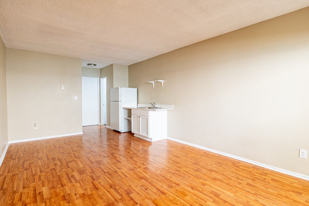 an empty living room with wood floors and a kitchen