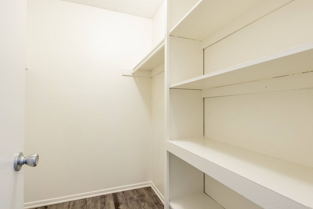 a walk in closet with white shelves and a door