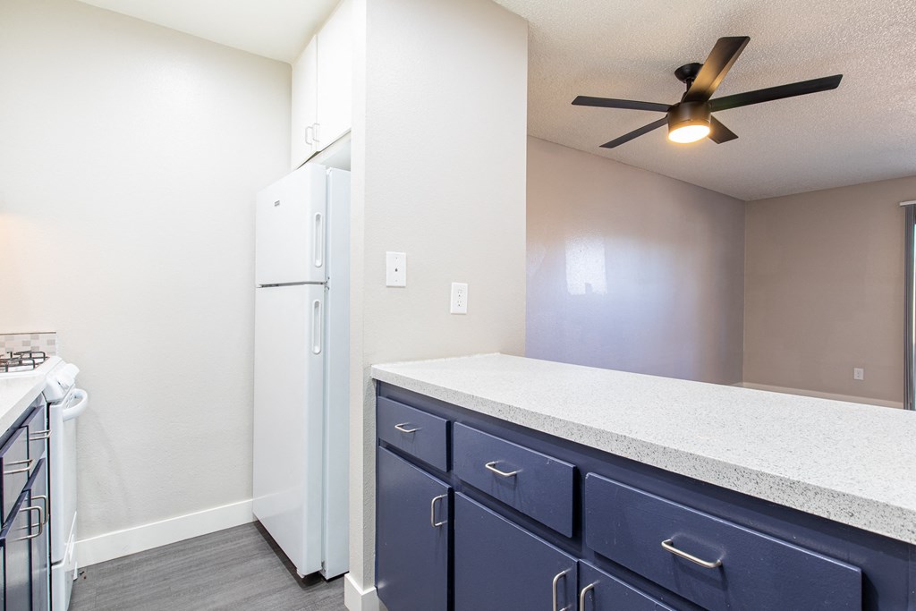 a kitchen with blue cabinets and a white refrigerator and a ceiling fan