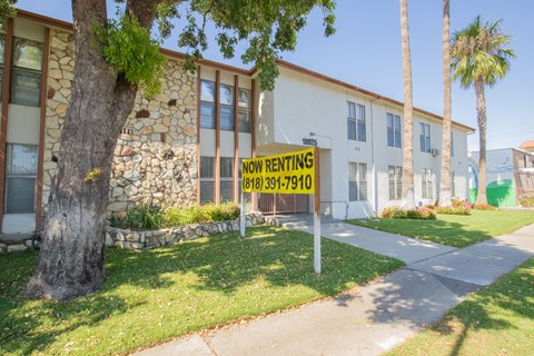 A sign in front of a building that says "NOW RENTING".