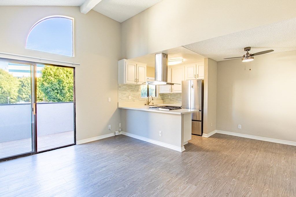 an empty living room with a kitchen and a sliding glass door